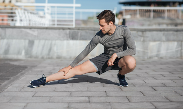 Cuerpo atlético y estilo de vida saludable. Hombre en cuclillas y haciendo ejercicios de piernas en la calle
 - Foto, imagen