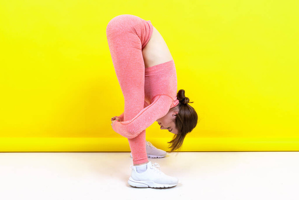 A young girl in a pink tracksuit trains on a yellow background - Photo, Image