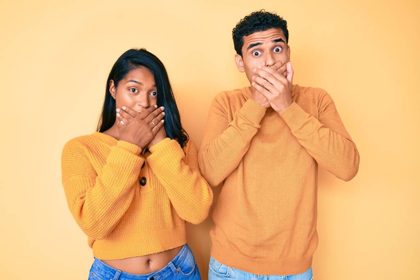 Beautiful latin young couple wearing casual clothes together shocked covering mouth with hands for mistake. secret concept.  - Фото, изображение
