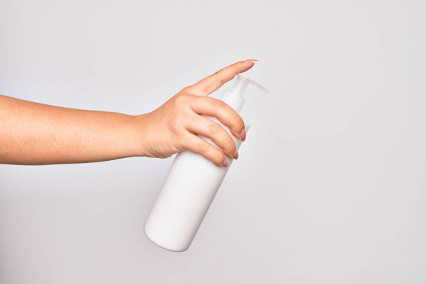 Hand of caucasian young woman holding bottle of body cream over isolated white background - Фото, зображення