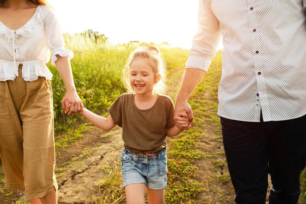 Happy parents and girl walking together in summer outside - Photo, Image