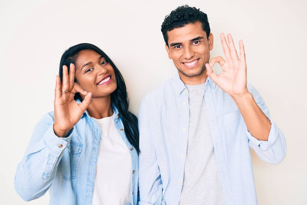 Krásná latinsky mladý pár na sobě ležérní oblečení s pozitivním úsměvem dělá v pořádku znamení s rukou a prsty. úspěšný výraz.  - Fotografie, Obrázek