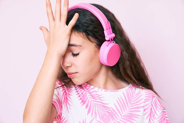 Enfant hispanique mignon écoutant de la musique à l'aide d'écouteurs surpris avec la main sur la tête pour erreur, rappelez-vous erreur. oublié, mauvais concept de mémoire.  - Photo, image