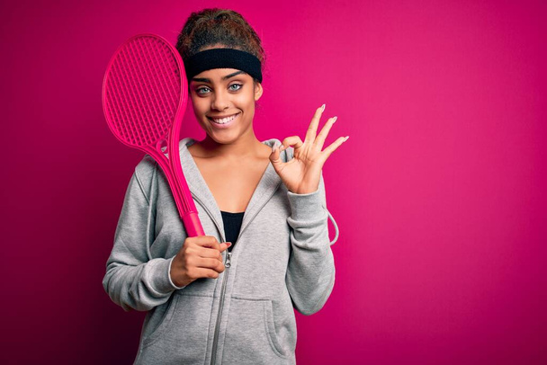 Fiatal afro-amerikai sportos nő teniszezik ütővel elszigetelt rózsaszín háttér csinál oké jel ujjakkal, kiváló szimbólum - Fotó, kép