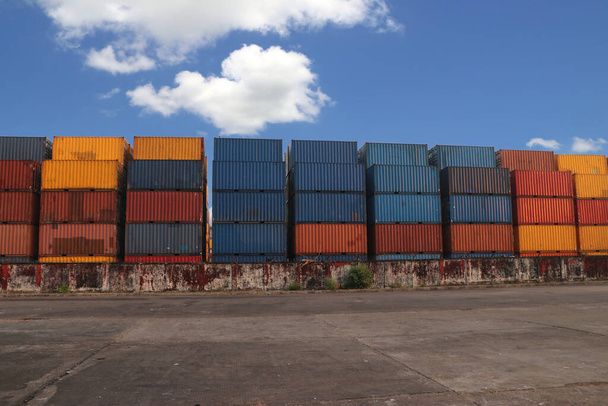 Scheepvaart Containers geplaatst als gelaagd in de opslagfaciliteit op blauwe hemel achtergrond. een voorwerp dat kan worden gebruikt om iets vast te houden of te vervoeren. - Foto, afbeelding