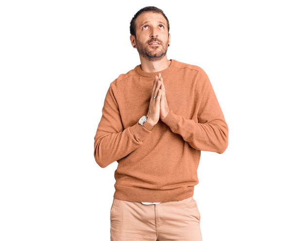 Jonge knappe man draagt casual kleding bedelend en biddend met handen samen met hoop uitdrukking op gezicht zeer emotioneel en bezorgd. bedelen.  - Foto, afbeelding