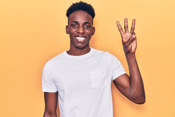 自信を持って幸せな笑みを浮かべている間、若いアフリカ系アメリカ人の男性は、カジュアルな服を着て指の数3で示すと指摘.  - 写真・画像
