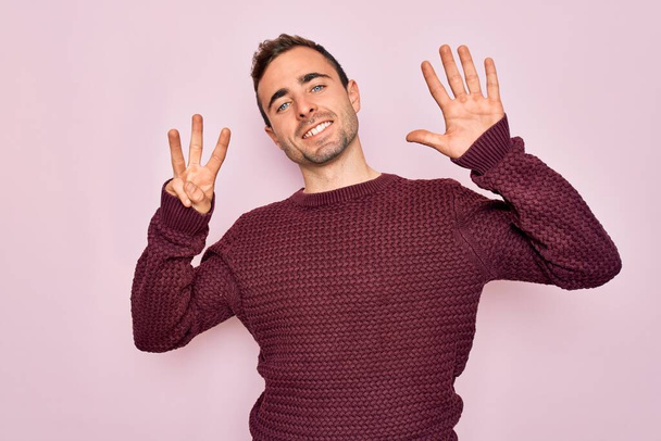 Young handsome man with blue eyes wearing casual sweater standing over pink background showing and pointing up with fingers number eight while smiling confident and happy. - Photo, Image
