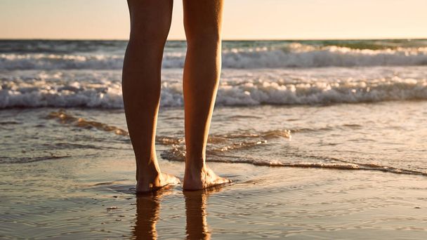 Gün batımında kumsalda kadınların bacakları. Plaj, tatil ve seyahat kavramı. - Fotoğraf, Görsel
