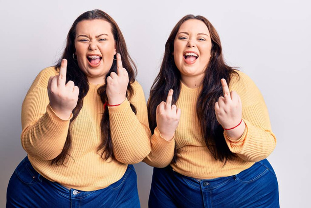 Young plus size twins wearing casual clothes showing middle finger doing fuck you bad expression, provocation and rude attitude. screaming excited  - Foto, Bild