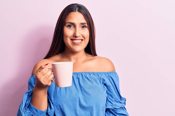 Young beautiful brunette woman drinking mug of coffee looking positive and happy standing and smiling with a confident smile showing teeth  - Photo, Image