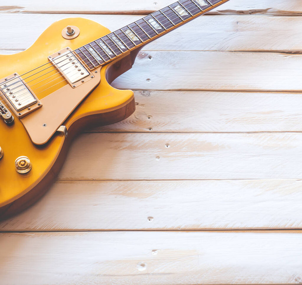 Mooie klassieke gouden elektrische gitaar op een witte houten tafel, met kopieerruimte. - Foto, afbeelding