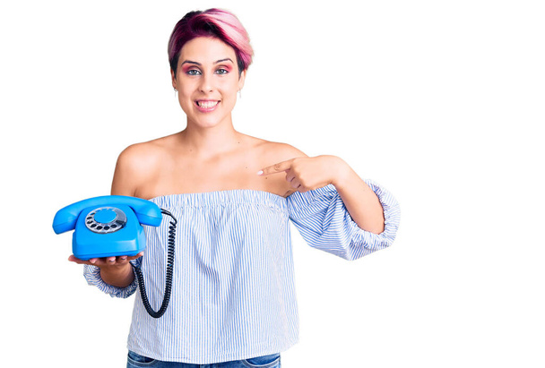 Young beautiful woman with pink hair holding vintage telephone pointing finger to one self smiling happy and proud  - Foto, Imagen