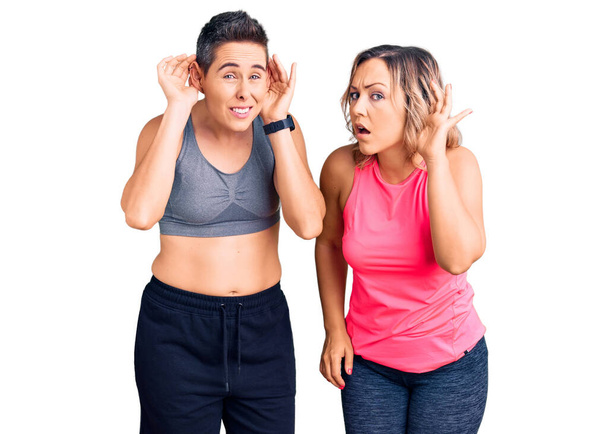 Pár žen ve sportovním oblečení, snažících se zaslechnout obě ruce na uchu, zvědavých na klepy. sluchový problém, hluchý  - Fotografie, Obrázek