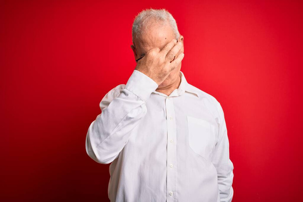 W średnim wieku przystojny hoary mężczyzna w luźnej koszuli i okularach na czerwonym tle zmęczony tarcie nosa i oczu uczucie zmęczenia i ból głowy. Koncepcja stresu i frustracji. - Zdjęcie, obraz