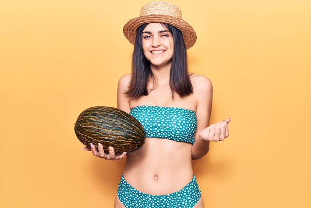 Joven hermosa chica con bikini sosteniendo melón gritando orgulloso, celebrando la victoria y el éxito muy emocionado con el brazo levantado
  - Foto, imagen