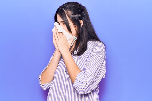 Young hispanic woman illness using paper handkerchief on nose. Standing over isoltated purple background - Foto, Bild