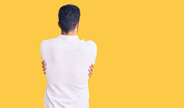 Young handsome hispanic man wearing casual clothes hugging oneself happy and positive from backwards. self love and self care  - Photo, Image