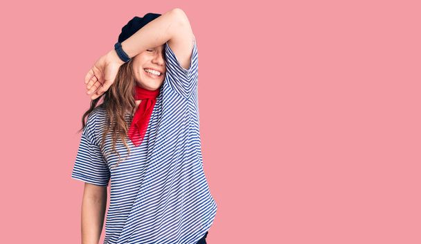 Young beautiful blonde woman wearing french beret and striped t-shirt covering eyes with arm smiling cheerful and funny. blind concept.  - Фото, зображення