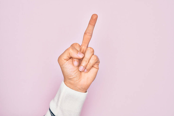 Hand of caucasian young man showing fingers over isolated pink background showing provocative and rude gesture doing fuck you symbol with middle finger - Photo, Image