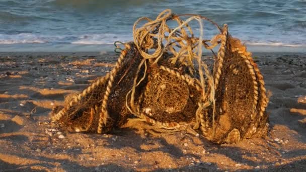 Régi használt piszkos halászhálók rozsdás dróttal, szemetet dobtak a tengerparti homokba. A környezetszennyezés fogalma. Mocskos homokos part. Mozgó hullámok kék víz háttér. Önkéntes koncepció - Felvétel, videó