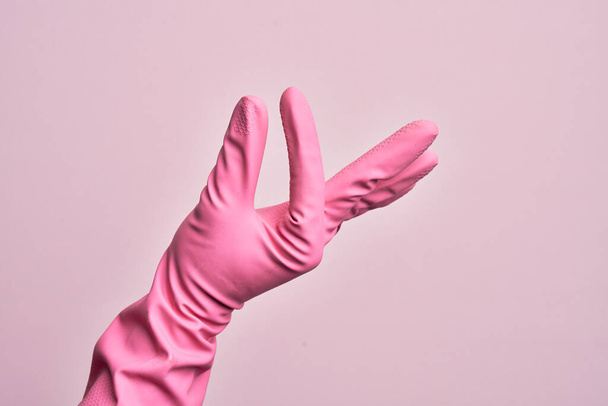 Main de jeune homme caucasien avec gant nettoyant sur fond rose isolé cueillette et prise chose invisible, tenant l'objet avec les doigts montrant de l'espace - Photo, image
