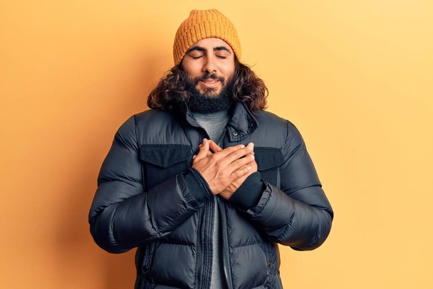 Jonge Arabier man draagt casual winterkleding glimlachend met handen op de borst met gesloten ogen en dankbaar gebaar op het gezicht. Gezondheidsconcept.  - Foto, afbeelding