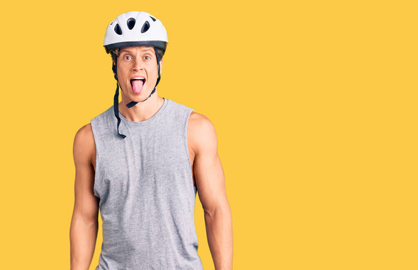Giovane bell'uomo che indossa il casco da bici attaccare la lingua fuori felice con espressione divertente. concetto di emozione.  - Foto, immagini