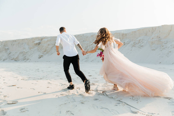 Історія кохання прекрасної пари в рожевій весільній сукні з букетом у пустелі Сахара, пісок, дюни. - Фото, зображення