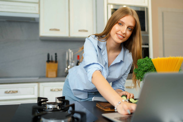 Young blonde woman with long hair using laptop in a kitchen - Foto, imagen