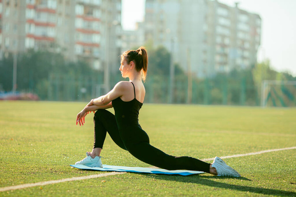 Beautiful fit woman doing leg stretching ,gymnastics , sportswear. Muscular slim attractive girl with flat belly in summer park outdoor. Body care, healthy, fitness, sporty life concept - 写真・画像