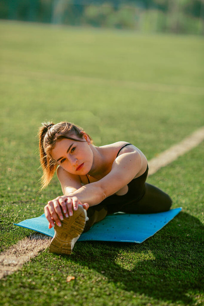 junges, gut aussehendes Mädchen in schwarzem Sportoutfit beim Stretching der Beine im Park - Foto, Bild