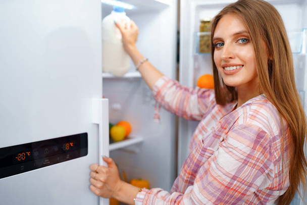 Portrait of a young blonde woman taking food from her fridge - Fotoğraf, Görsel