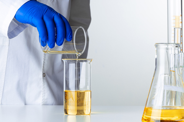 Scientist or doctor in blue gloves pouring some yellow liquid into a flask - Fotó, kép