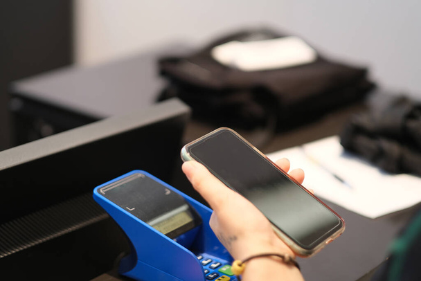 close up one hand holding smart phone above reader at the point of sale. contactless payment concept - Foto, immagini