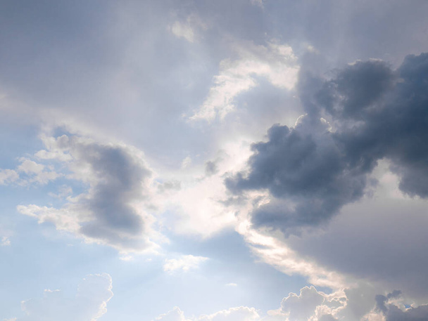 Sonnenstrahlen brechen durch eine große Wolke, die sich am Himmel gebildet hat, umgeben von diffusen Wolken und einem blauen Himmel im Hintergrund - Foto, Bild