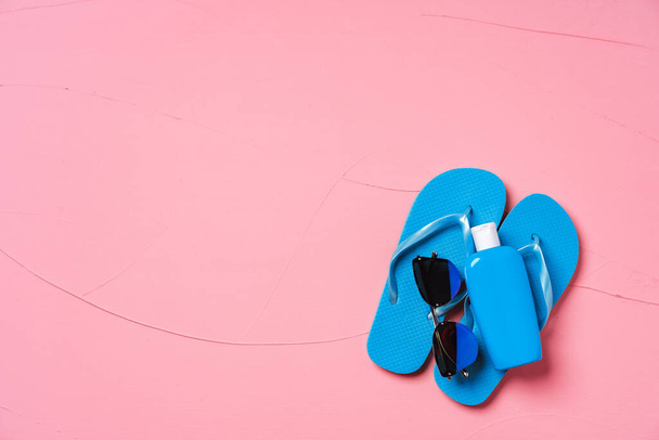 Blue flip-flops with sunscreen and sunglasses on pink background - Foto, Imagem
