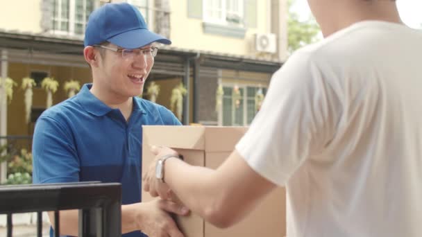 郵便配達の若い男は、顧客に送信するための小包ボックスを保持します,アジアの男性は、屋外で配達小包を受け取るために携帯電話のQRコードを介して署名し、支払う. - 映像、動画