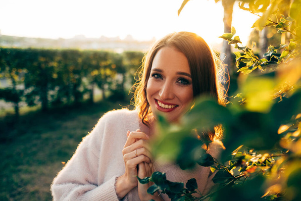 a girl in a light pink sweater smiles at the sunset - Foto, Imagen