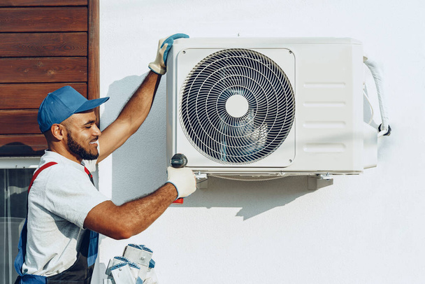 Repairman in uniform installing the outside unit of air conditioner - 写真・画像