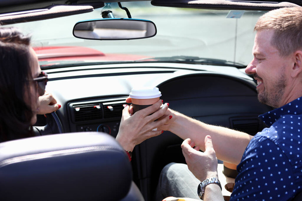 Man and woman are sitting in car smiling and holding glass of coffee. - 写真・画像