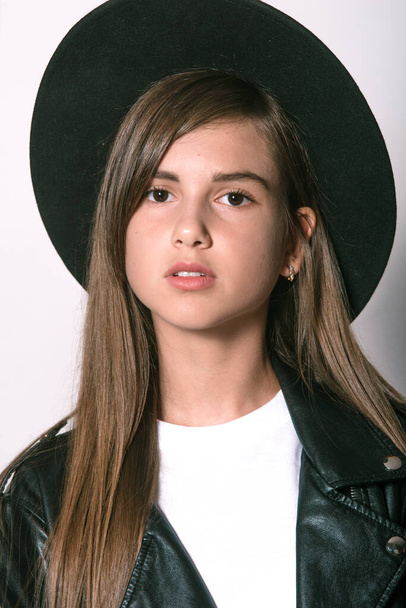 A teenage girl in a trendy leather jacket and an even hat on a white background. Teenage fashion. Street fashion. Beauty and fashion - Fotoğraf, Görsel