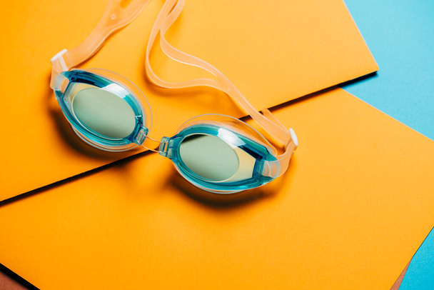 Sarı geometrik arka planda lastik kayışlı mavi yüzme gözlükleri. Hiç kimse, ürün konsepti - Fotoğraf, Görsel