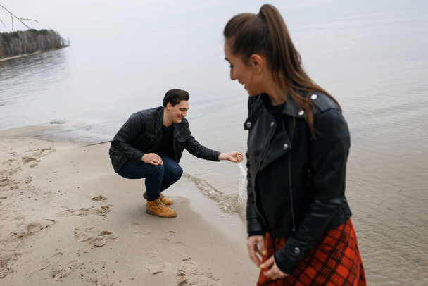 giovane coppia in giacche nere che si abbraccia e posa sulla spiaggia. - Foto, immagini