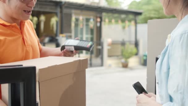 Mladý poštovní kurýr muž drží balíčky pro odeslání zákazníkovi, asijské ženy podepisovat a platit přes QR kód na mobilním telefonu pro příjem doručovaných balíků venku. 4k Zpomalený pohyb. - Záběry, video