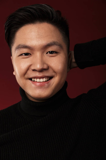 Image of cheerful asian man smiling and looking at camera isolated over burgundy background - Foto, Bild