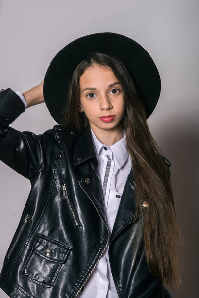 A teenage girl in a trendy leather jacket and an even hat on a white background. Teenage fashion. Street fashion. Beauty and fashion - Foto, immagini