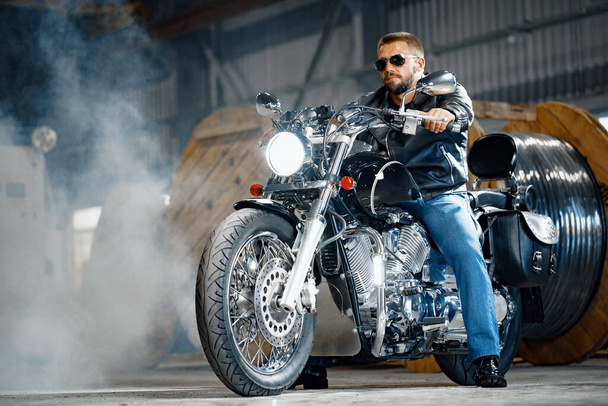 Bearded motorcyclist in black leather clothing with his motorbike - Foto, afbeelding