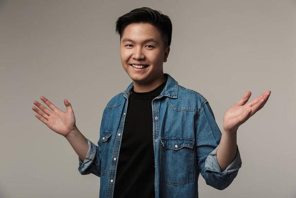 Image of cheerful handsome asian man smiling with throwing up hands isolated over gray background - Foto, Bild