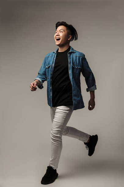 Image of delighted handsome asian man laughing and running isolated over gray background - Φωτογραφία, εικόνα